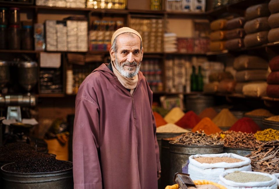 Smiling man in traditional robe at a vibrant spice market in Morocco