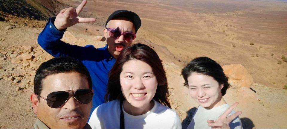 Travelers taking a group selfie during a Morocco desert tour with rocky mountain scenery
