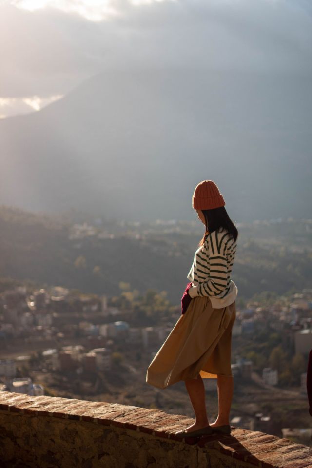 Woman watching the sunset over the blue medina of Chefchaouen from a hillside wall