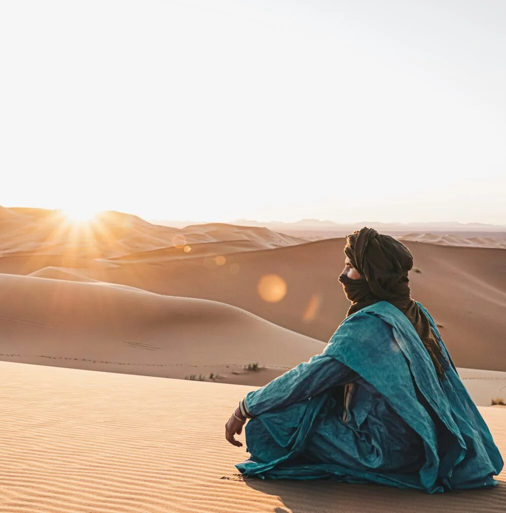 Traveler sitting on golden sand dunes at sunset in the Mhamid Desert near Erg Chigaga, southern Morocco.