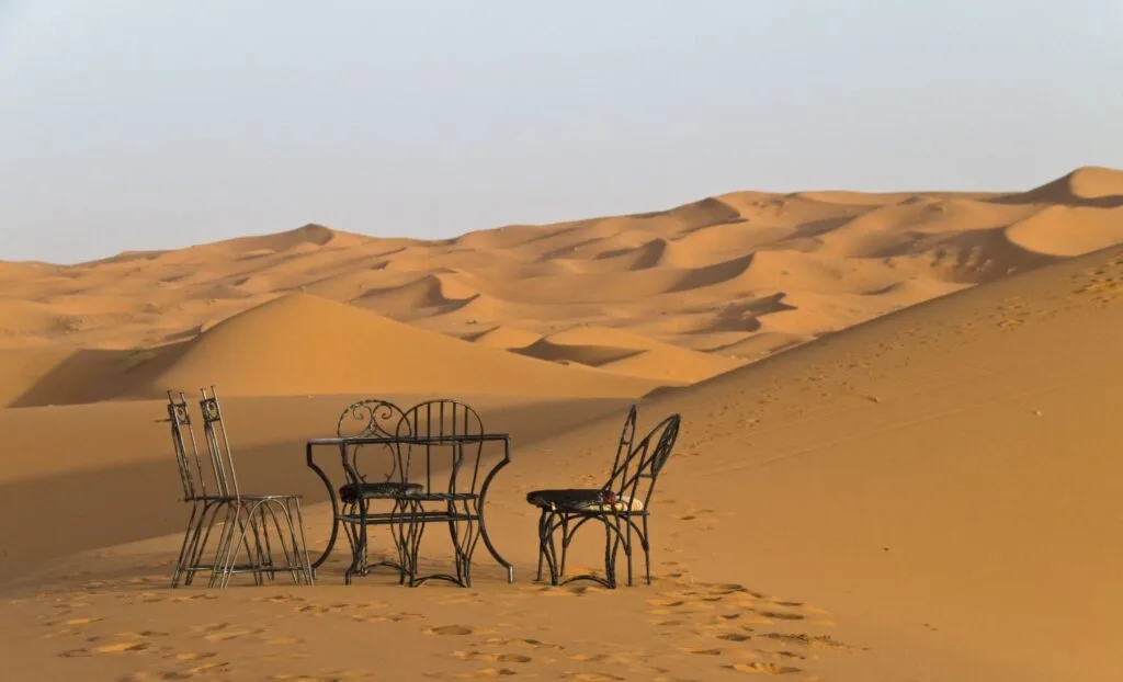 Sweeping aerial view of the golden Erg Chebbi sand dunes in Merzouga, Morocco, with rippled sandy crests and warm desert light casting deep shadows across the vast Sahara landscape.