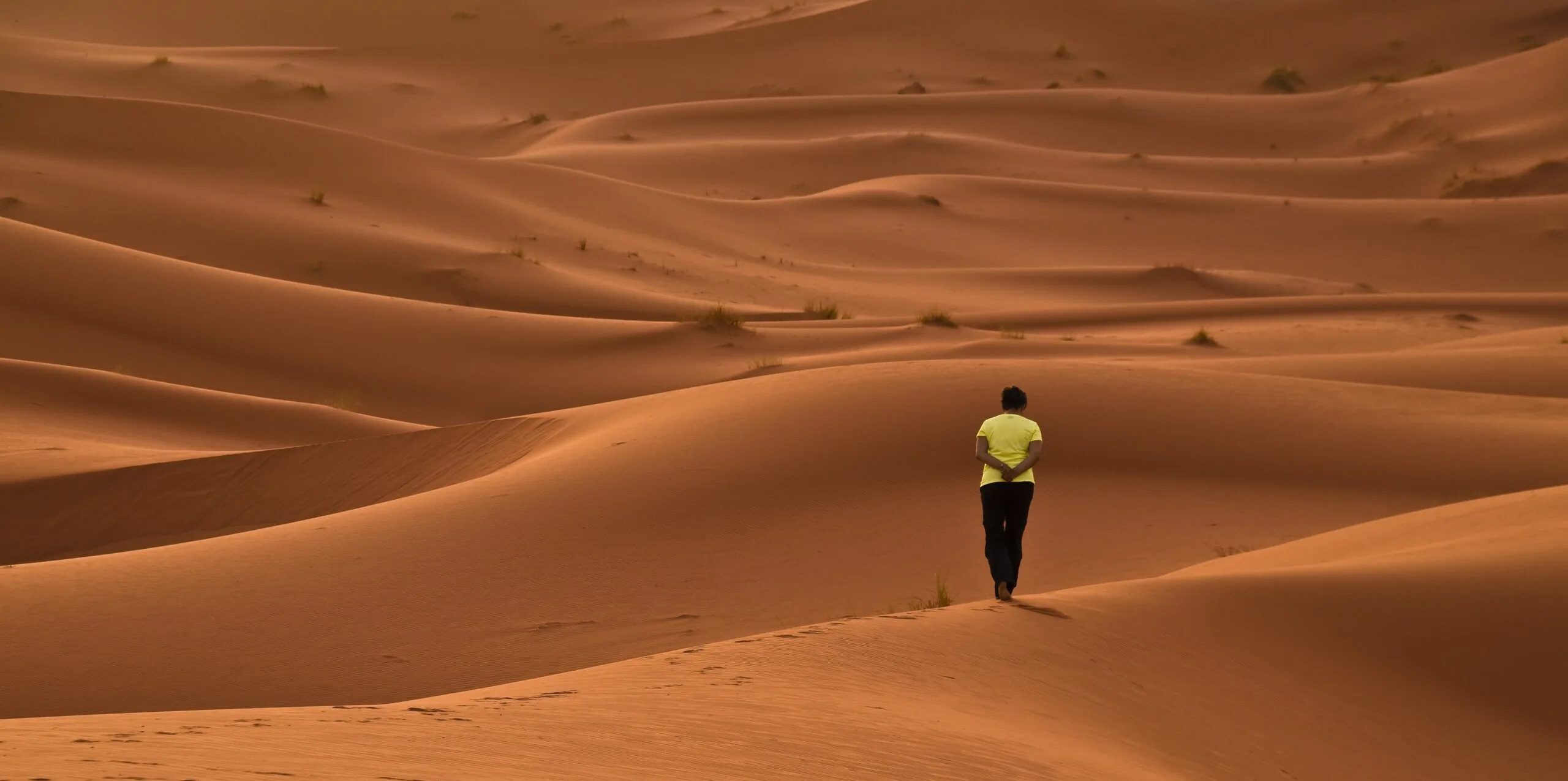 Traveler walking through Erg Chebbi dunes in Merzouga Sahara, Morocco