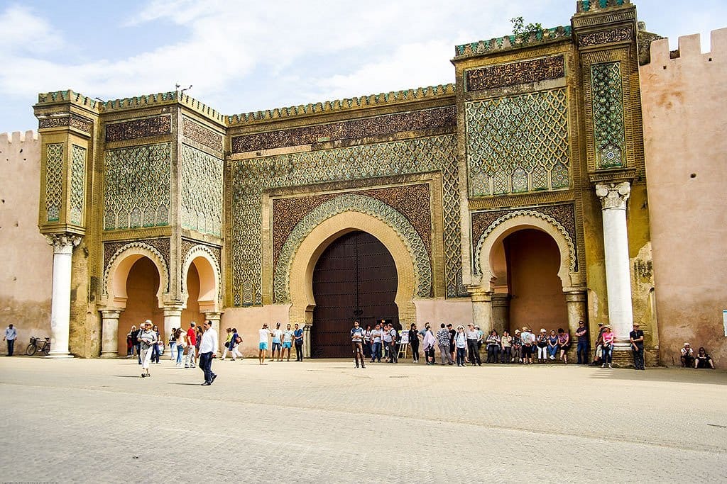 The grand Bab Mansour gate in Meknes, Morocco, an elaborately decorated 18th-century triumphal arch featuring intricate zellige tilework, carved stucco arabesques, and towering horseshoe arches, located near the mausoleum of Sultan Moulay Ismail.