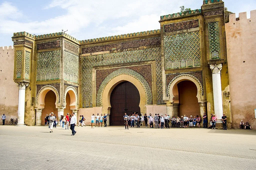 The grand Bab Mansour gate in Meknes, Morocco, an elaborately decorated 18th-century triumphal arch featuring intricate zellige tilework, carved stucco arabesques, and towering horseshoe arches, located near the mausoleum of Sultan Moulay Ismail.