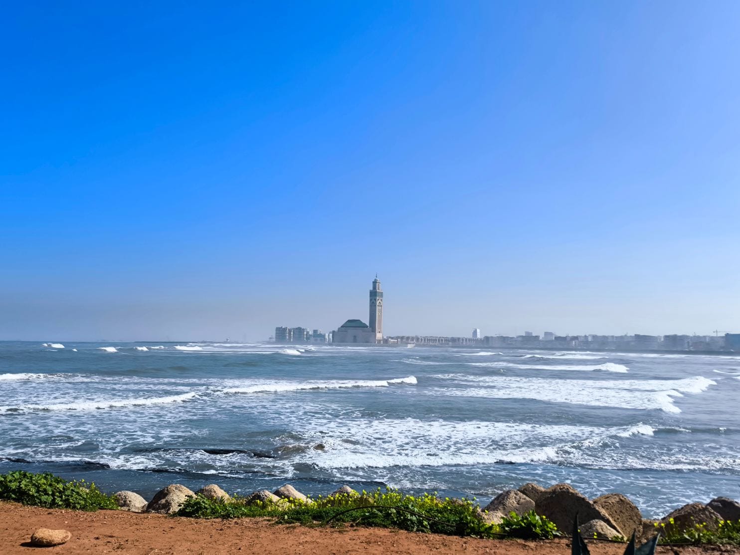 Majestic view of the Hassan II Mosque in Casablanca, Morocco, rising dramatically above the Atlantic Ocean waters, with its towering minaret, ornate Moorish façade, and vast marble esplanade reflecting the golden light over the sea.