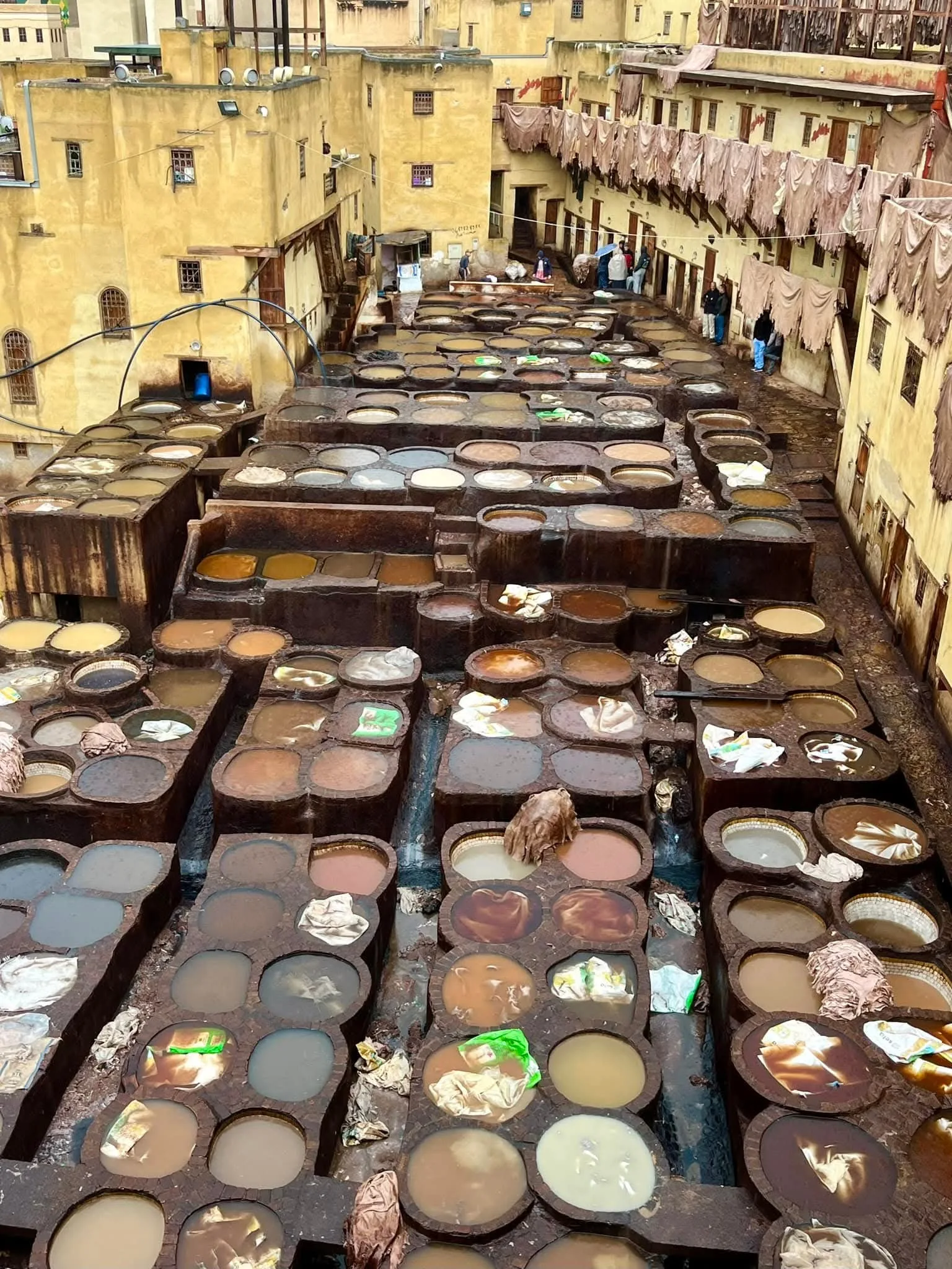 An overhead view of the famous Chouara tannery in Fes, Morocco, showcasing the rows of circular stone vats filled with vibrant colored dyes and natural pigments used in the centuries-old traditional leather tanning process.
