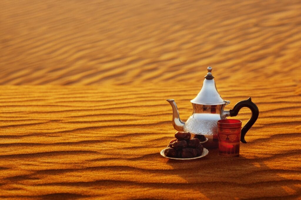 Traditional Moroccan teapot on golden Sahara dunes at sunset